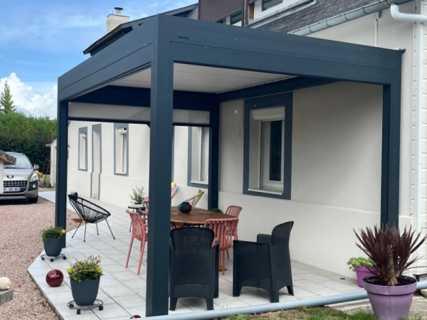 Pergola bioclimatique anthracite, store blanc, terrasse grise et table ronde bois