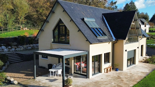 Maison crépi : pergola bioclimatique anthracite, baies alu, lucarnes et volets roulants