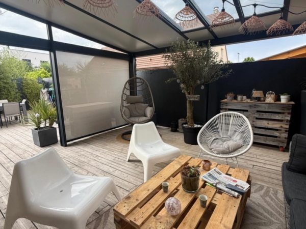 Pergola anthracite toiture fixe, store vertical beige, terrasse bois et fauteuils blancs