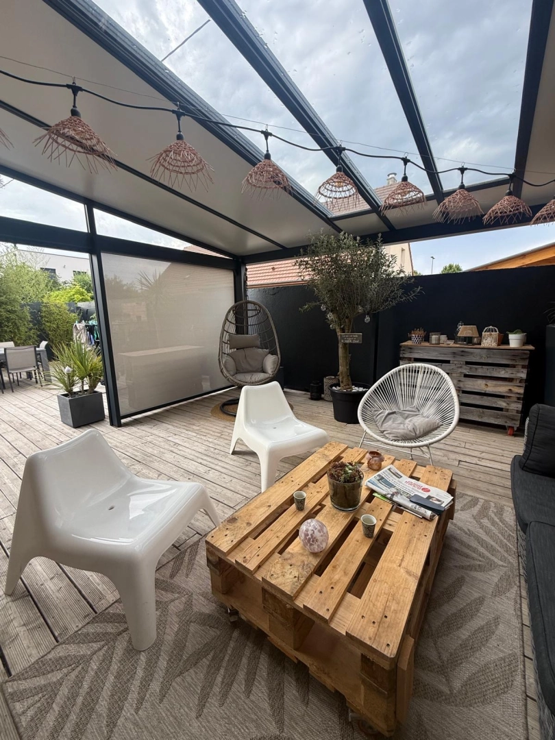 Pergola anthracite toiture fixe, store vertical beige, terrasse bois et fauteuils blancs