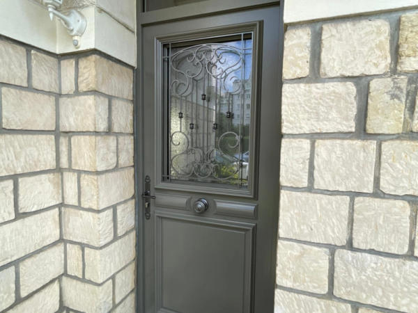 Porte d'entrée anthracite, vitrage avec grille fer forgé, mur pierre beige et imposte