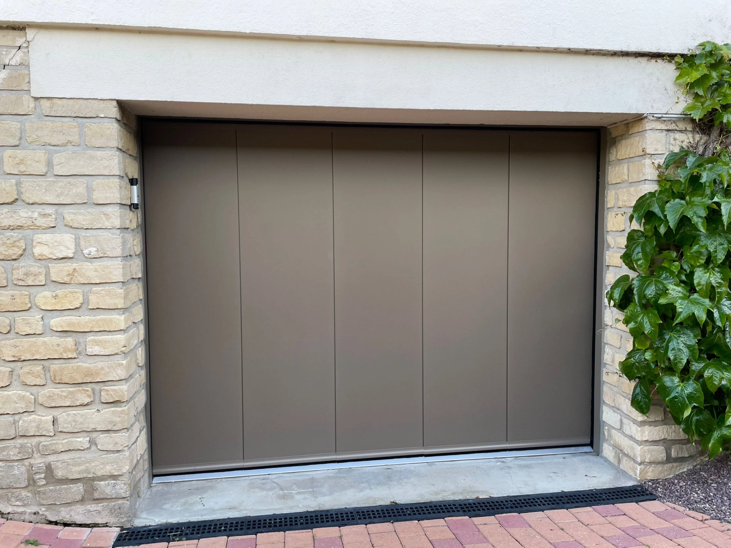 Porte de garage latérale bronze cinq panneaux, seuil pierre et pavés roses