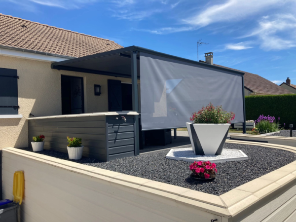 Pergola anthracite adossée, store vertical gris déroulé, terrasse gravier et jardinières