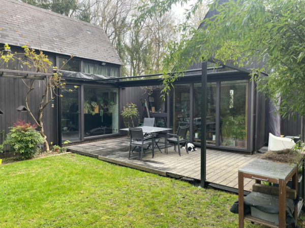 Maison bardage bois noir, baies vitrées noires, extension verre et terrasse bois