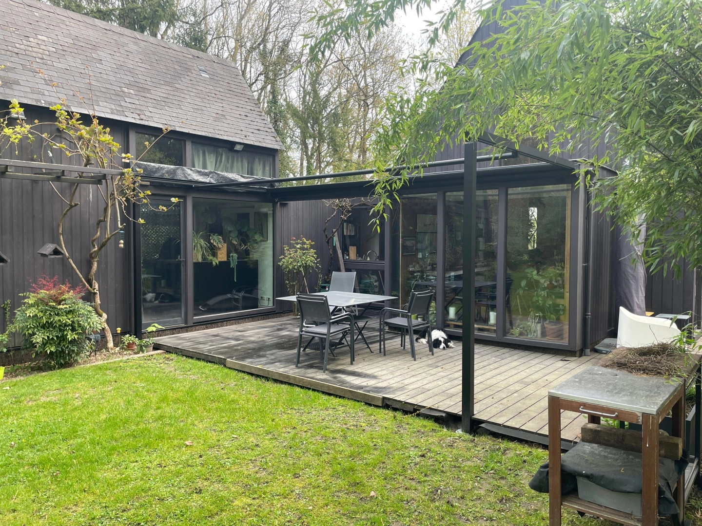 Maison bardage bois noir, baies vitrées noires, extension verre et terrasse bois