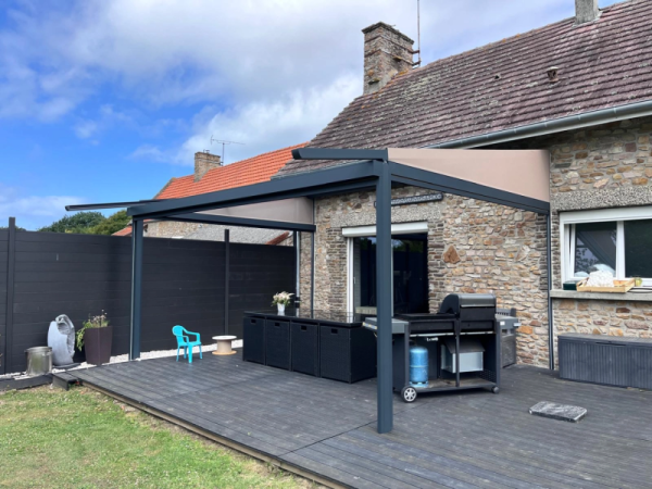 Storgola anthracite, toile rétractable beige, terrasse bois gris devant maison en pierre
