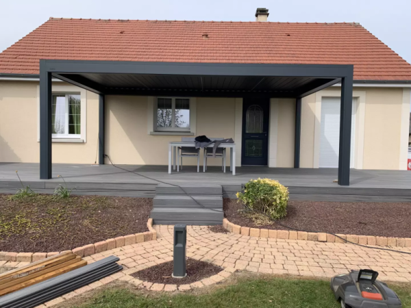 Pergola bioclimatique anthracite sur terrasse composite grise, maison enduit beige
