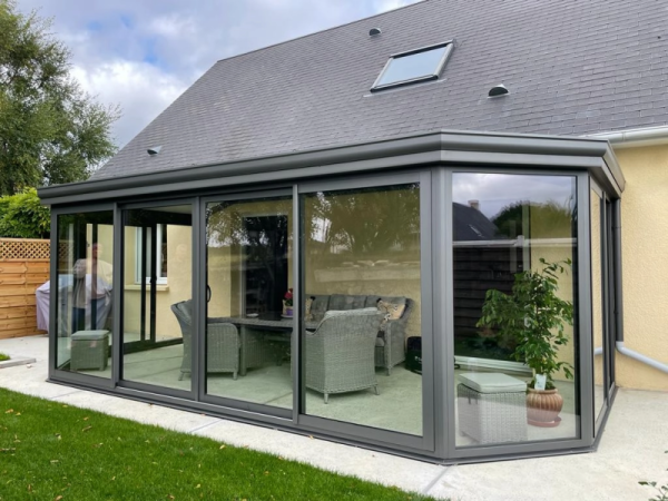 Véranda alu gris anthracite toit plat, baies coulissantes, muret briques et dalle béton