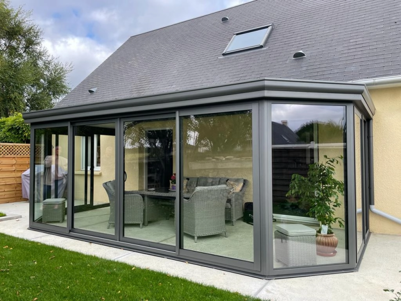 Véranda alu gris anthracite toit plat, baies coulissantes, muret briques et dalle béton