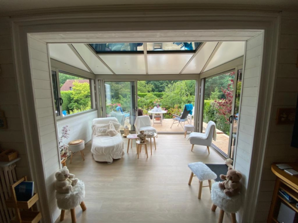 Intérieur véranda, baies coulissantes beige, verrière toit, parquet clair, jardin
