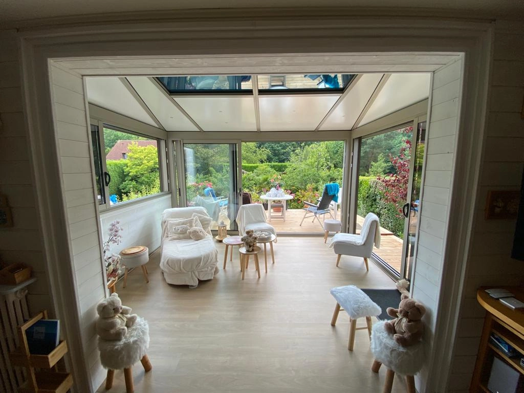 Intérieur véranda, baies coulissantes beige, verrière toit, parquet clair, jardin