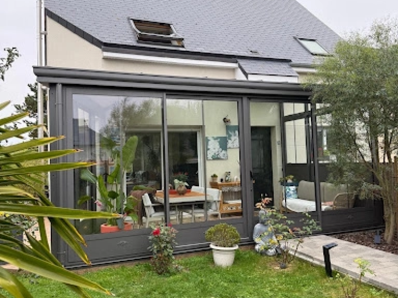 Véranda anthracite jardin : salle à manger blanche et canapé, baies coulissantes