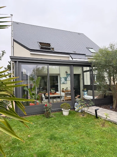 Véranda anthracite jardin : salle à manger blanche et canapé, baies coulissantes