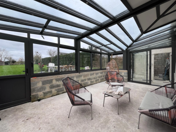 Véranda alu anthracite toit vitré, soubassement parpaings, dalle béton, mobilier
