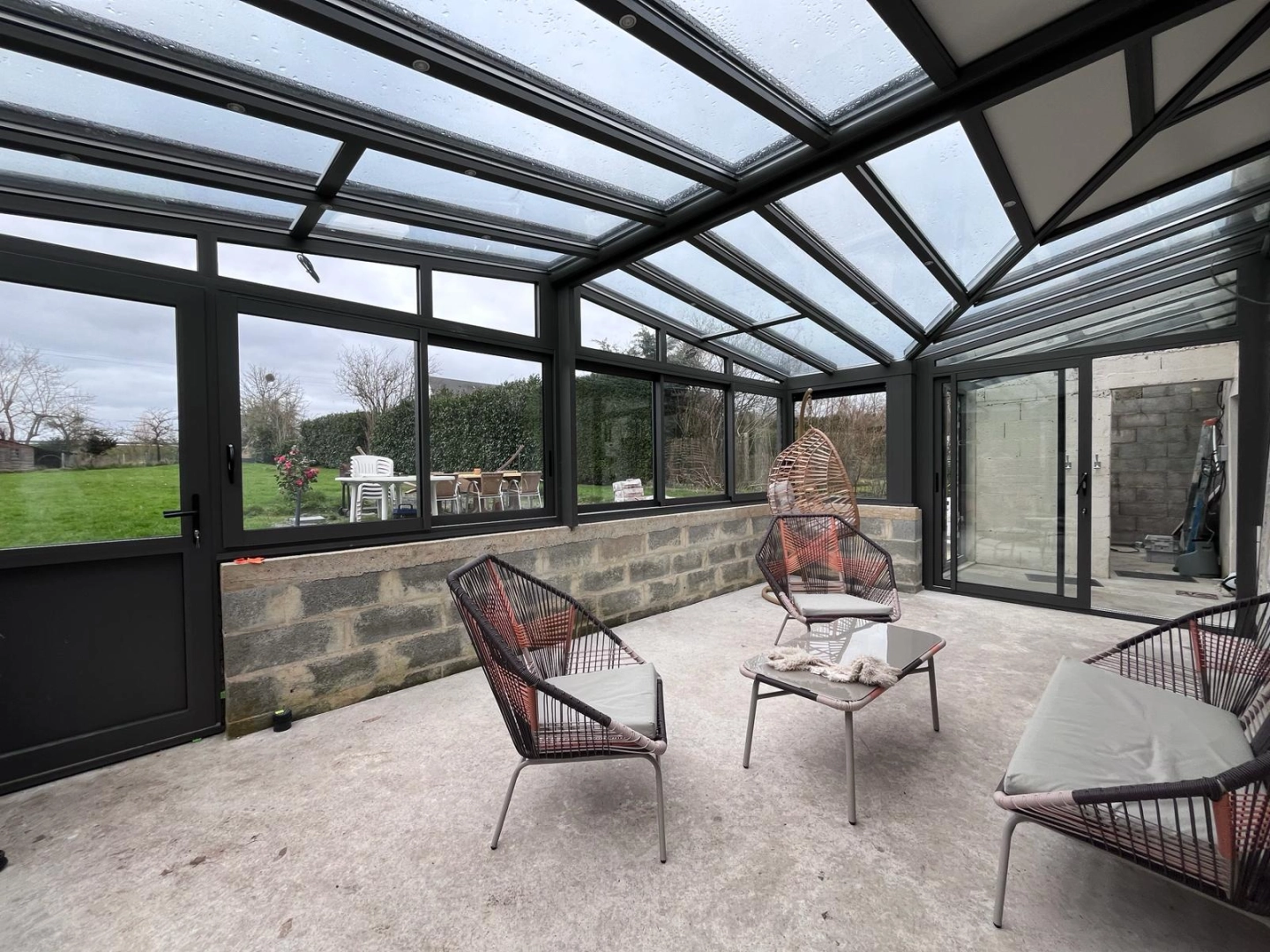 Véranda alu anthracite toit vitré, soubassement parpaings, dalle béton, mobilier