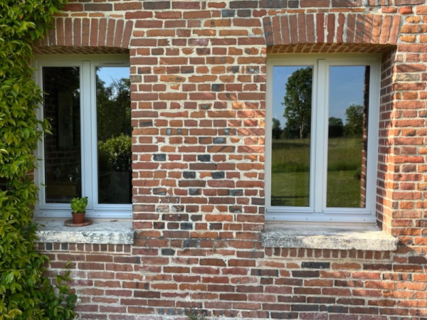 Deux fenêtres blanches posées dans mur briques rouges avec linteaux en arc