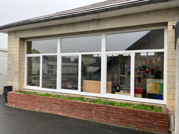 Triple menuiserie blanche PVC sur façade pierre d'un bâtiment scolaire, jardinière briques