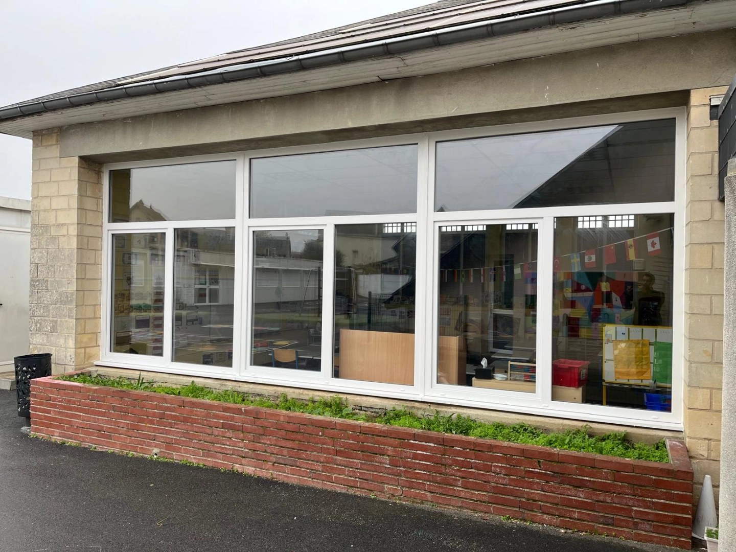 Triple menuiserie blanche PVC sur façade pierre d'un bâtiment scolaire, jardinière briques