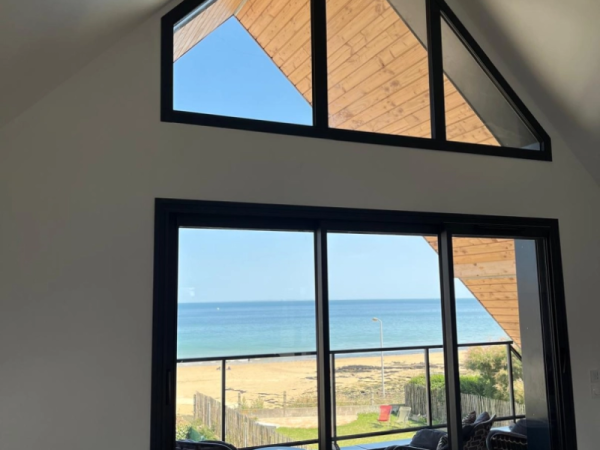 Baie coulissante alu noire et vitrages en pinacle, vue mer et plage depuis l'intérieur