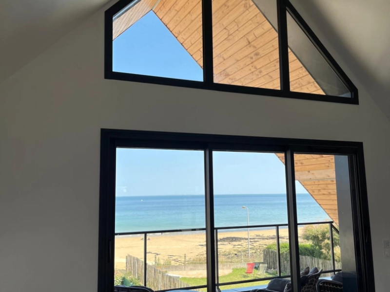 Baie coulissante alu noire et vitrages en pinacle, vue mer et plage depuis l'intérieur