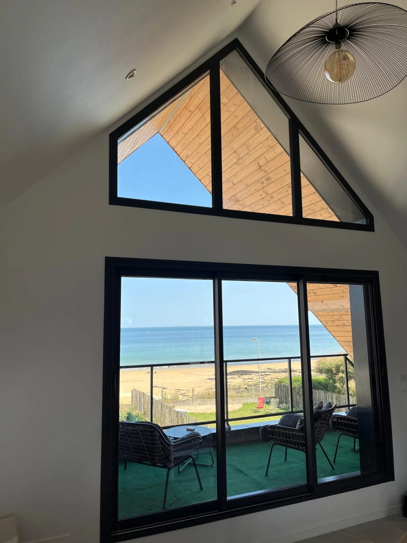 Baie coulissante alu noire et vitrages en pinacle, vue mer et plage depuis l'intérieur