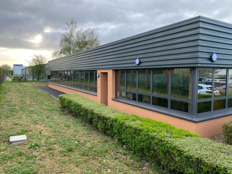 Bâtiment tertiaire : fenêtres alu anthracite sous bardage métal gris et enduit terracotta