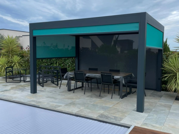 Pergola bioclimatique anthracite, store vertical turquoise, terrasse pierre et piscine couverte