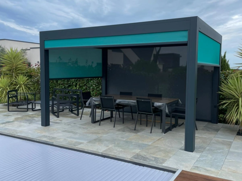 Pergola bioclimatique anthracite, store vertical turquoise, terrasse pierre et piscine couverte