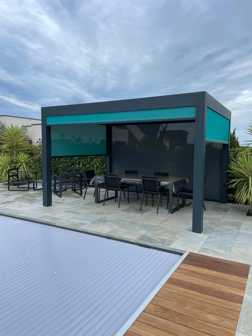 Pergola bioclimatique anthracite, store vertical turquoise, terrasse pierre et piscine couverte