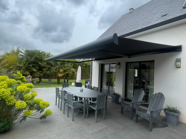Store banne coffre anthracite déployé, terrasse dalles, jardin palmiers