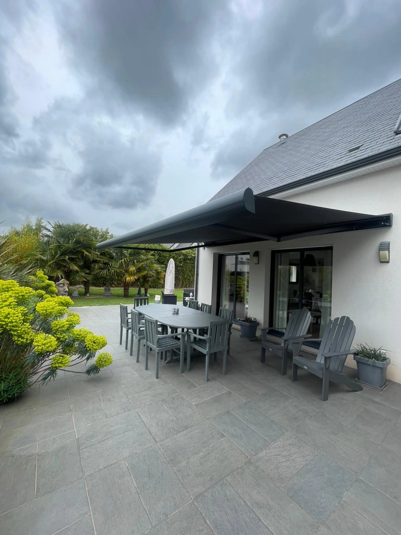 Store banne coffre anthracite déployé, terrasse dalles, jardin palmiers