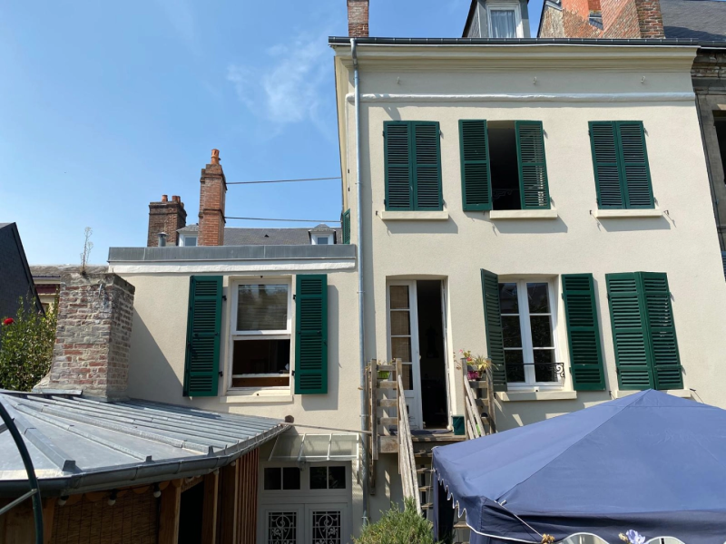 Façade rénovée : fenêtres blanches et volets persiennés vert foncé, lucarnes
