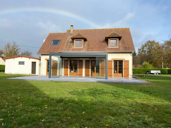 Pergola anthracite parois vitrées, terrasse dalles grises, maison tuiles et volets