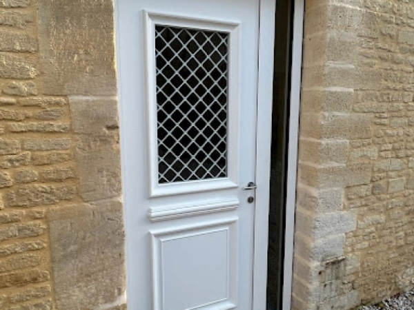 Porte d'entrée blanche grille losanges dans mur pierre beige traditionnel