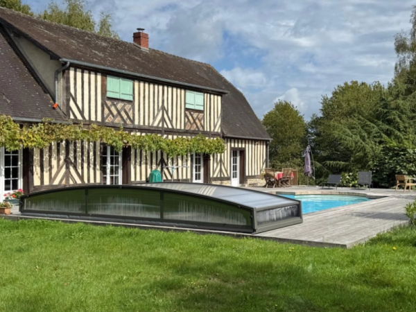 Abri piscine bas télescopique anthracite sur terrasse bois, maison colombages