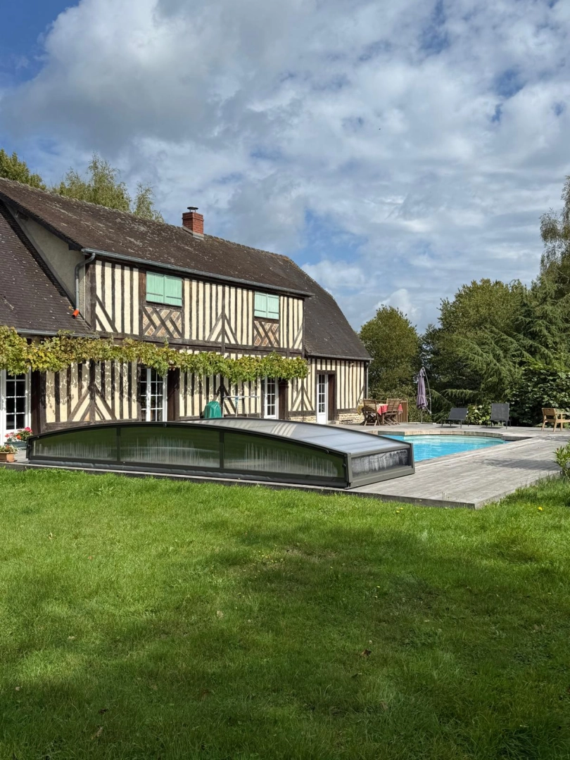 Abri piscine bas télescopique anthracite sur terrasse bois, maison colombages