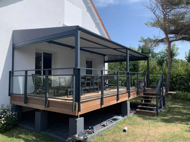Terrasse bois sur pilotis, pergola anthracite, garde-corps vitré, maison blanche