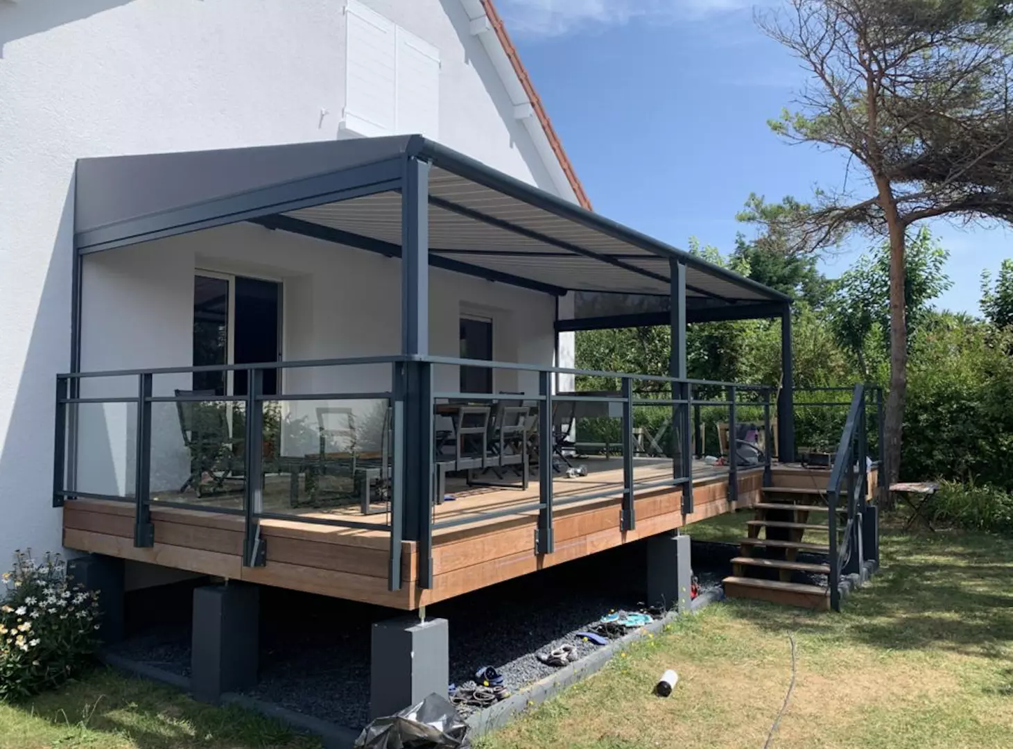 Terrasse bois sur pilotis, pergola anthracite, garde-corps vitré, maison blanche