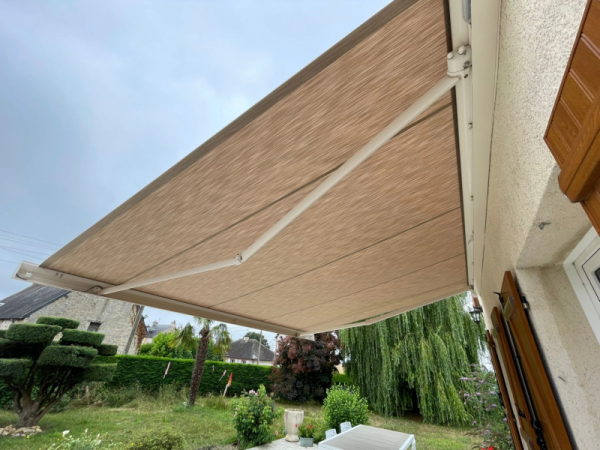 Store banne beige rayé déployé, bras blancs, jardin topiaire et volets bois