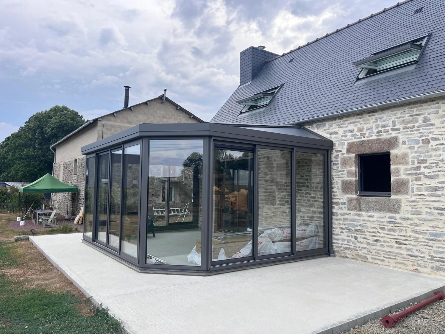 Véranda anthracite double toit sur dalle béton neuve, sacs isolant visibles