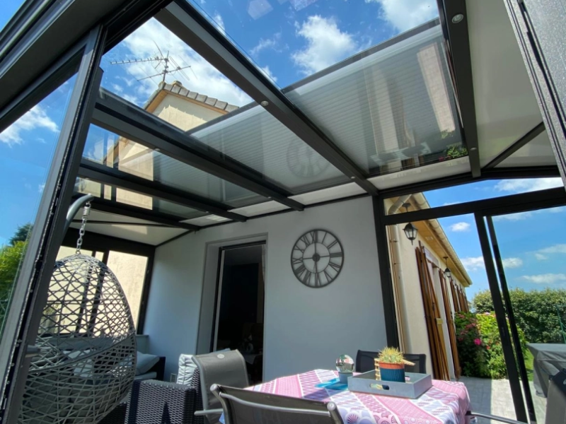 Véranda anthracite toit verre, stores roulants intégrés, salon et horloge murale