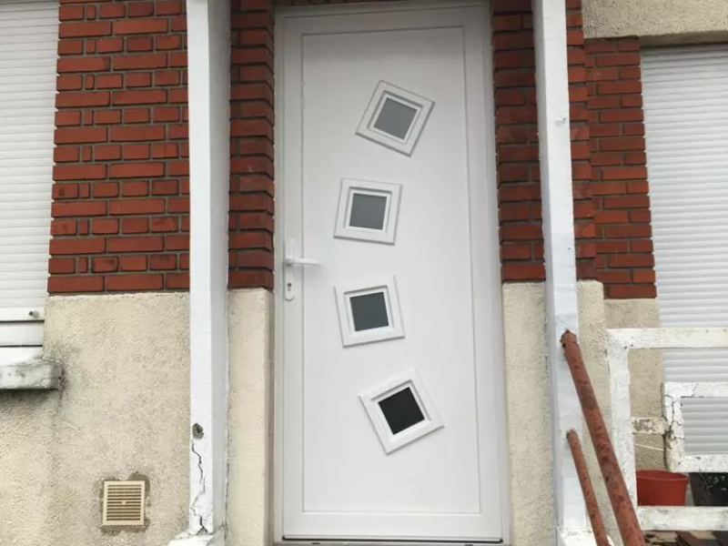 Porte d'entrée PVC blanche à quatre hublots carrés, façade briques rouges et enduit beige
