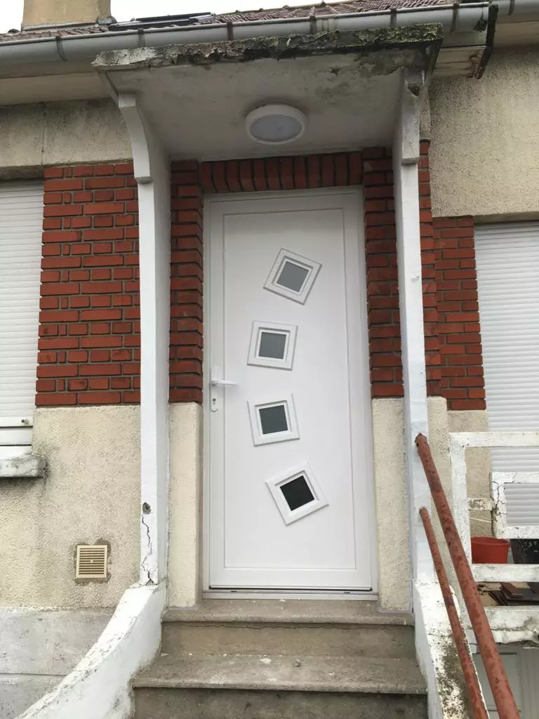 Porte d'entrée PVC blanche à quatre hublots carrés, façade briques rouges et enduit beige