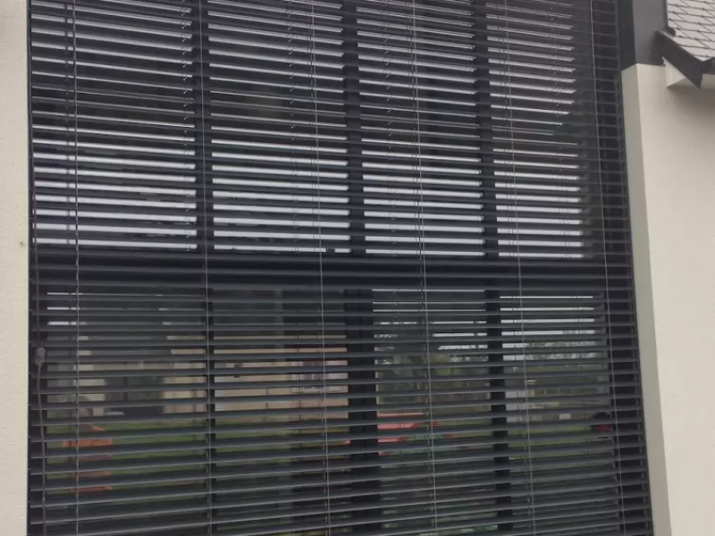 Brise-soleil orientable alu anthracite sur grande baie vitrée, façade enduit crème