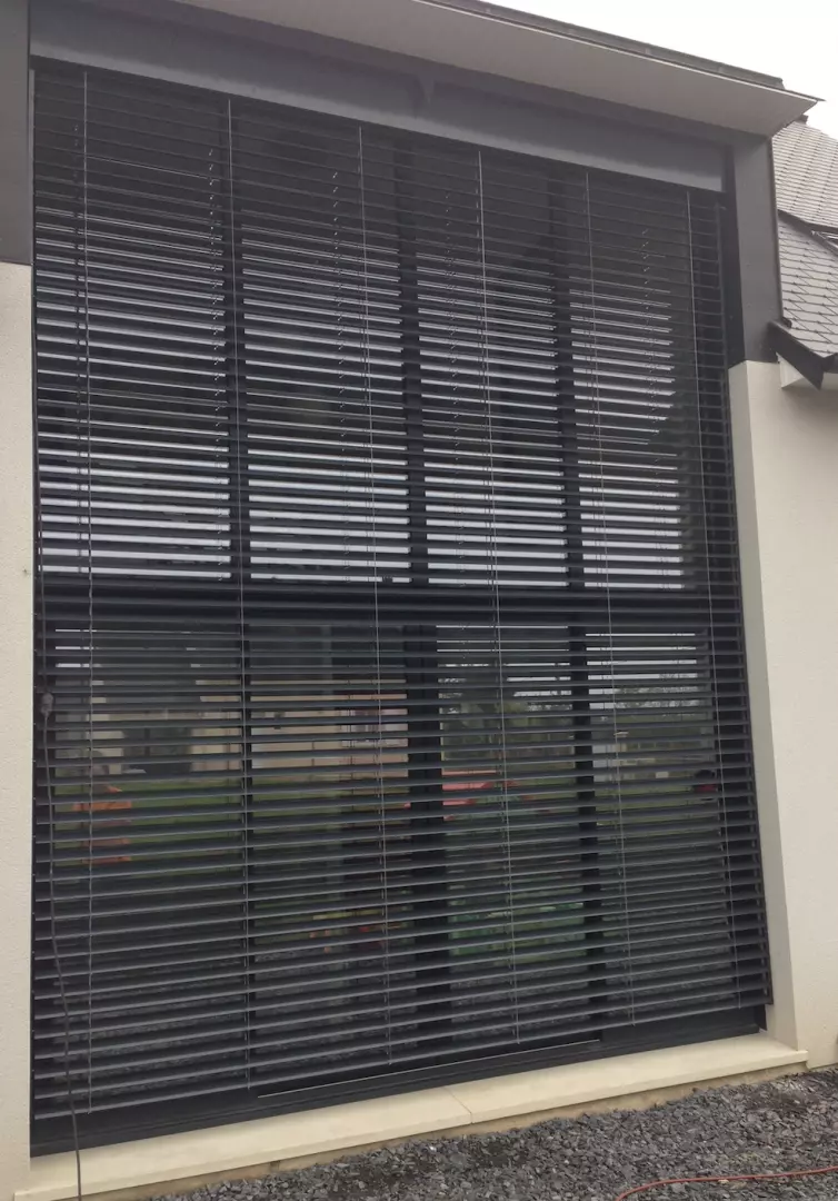 Brise-soleil orientable alu anthracite sur grande baie vitrée, façade enduit crème