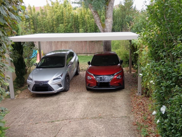 Carport alu blanc toit plat abritant deux SUV sur allée gravier et jardin verdoyant