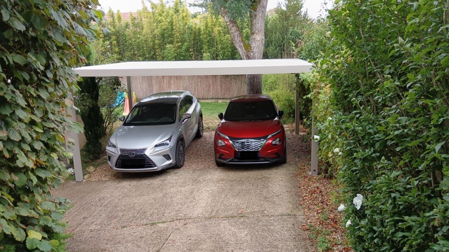 Carport alu blanc toit plat abritant deux SUV sur allée gravier et jardin verdoyant