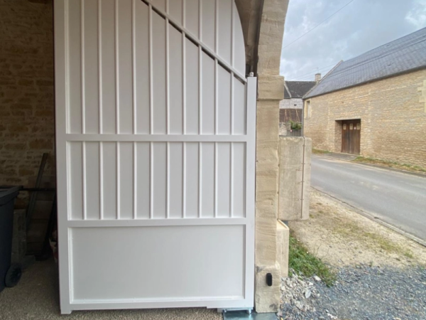 Portail blanc cintré à lames verticales intégré dans mur en pierre de taille beige