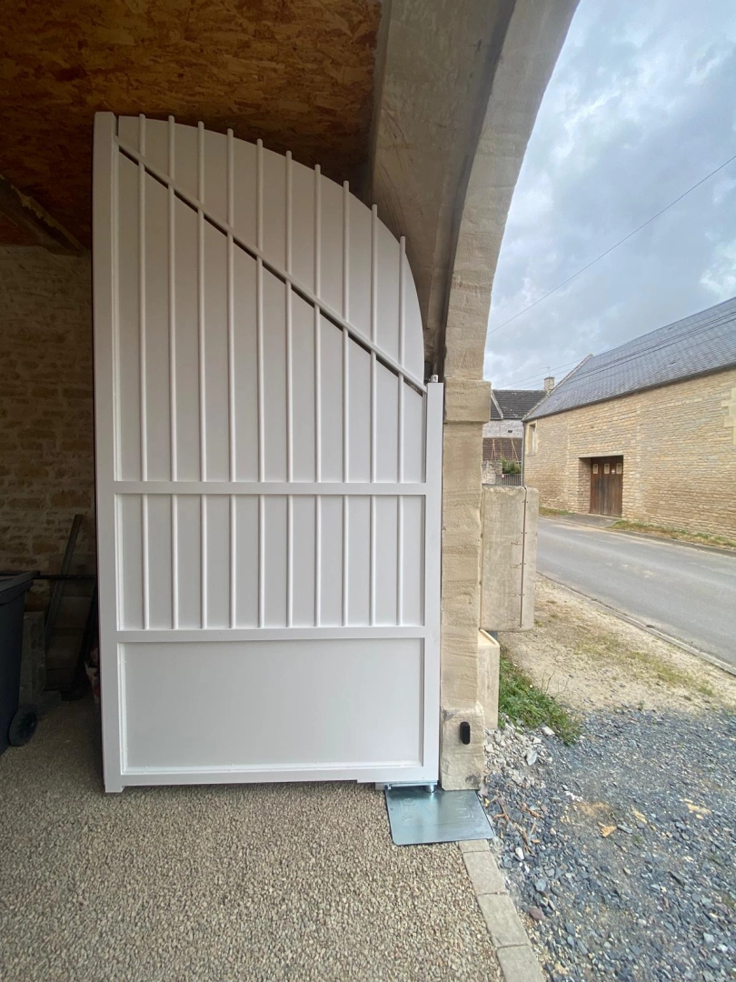 Portail blanc cintré à lames verticales intégré dans mur en pierre de taille beige