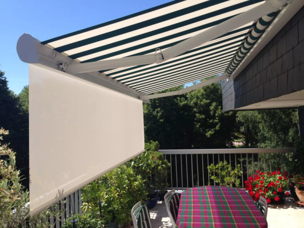 Store banne rayures vert et blanc, lambrequin blanc déroulé, terrasse avec table et géraniums